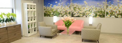 A cozy lounge area featuring a pink sofa, gray chairs, and a beautiful flower arrangement against a backdrop of floral artwork.