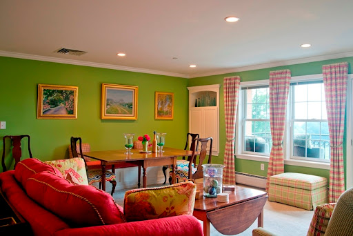 A vibrant living room featuring green walls and a cozy seating area, complemented by decorative paintings and a dining table.