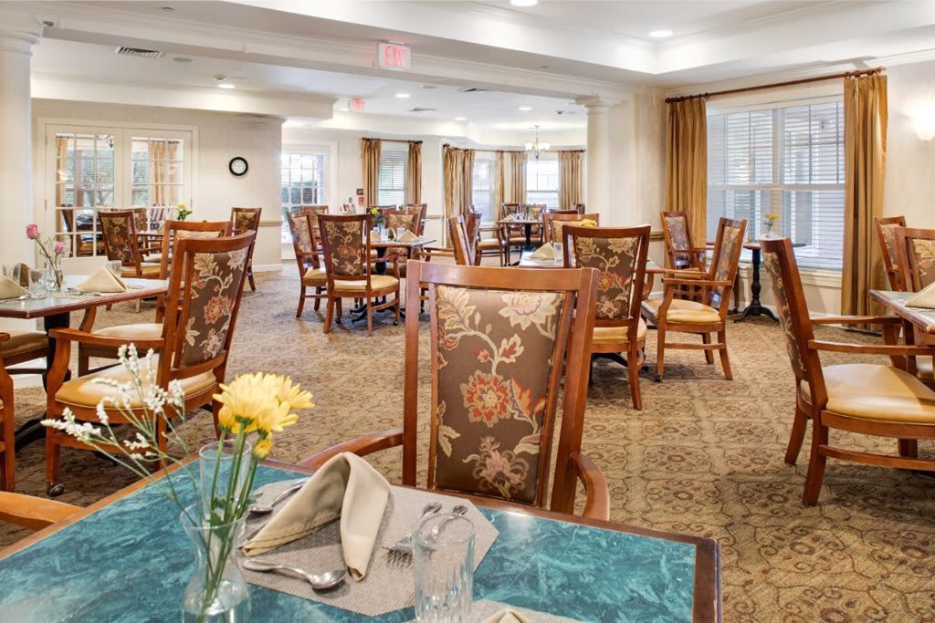 A spacious dining room with elegantly set tables and chairs, featuring floral decorations.