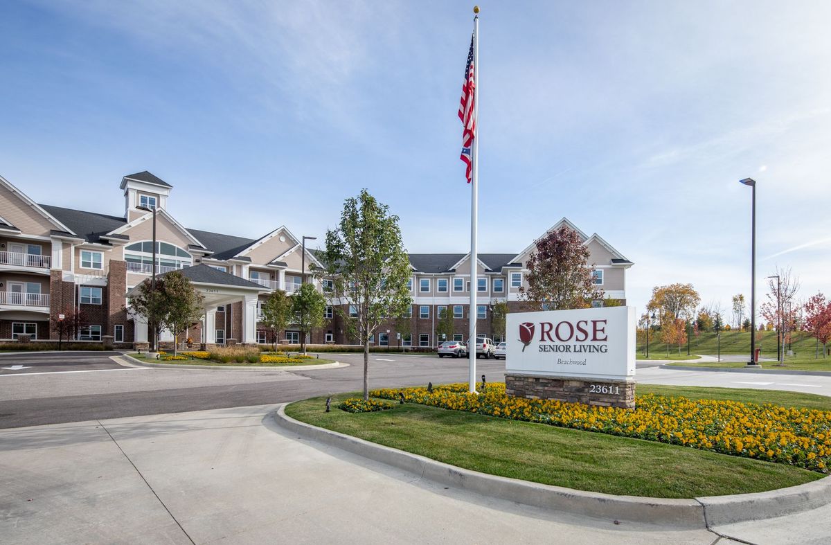 An exterior view of a building with a sign reading 'Rose Senior Living' and an American flag nearby.