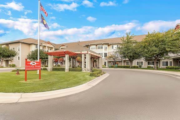 A well-maintained building with a welcoming entrance, surrounded by manicured landscaping and adorned with flags, under a blue sky with scattered clouds.