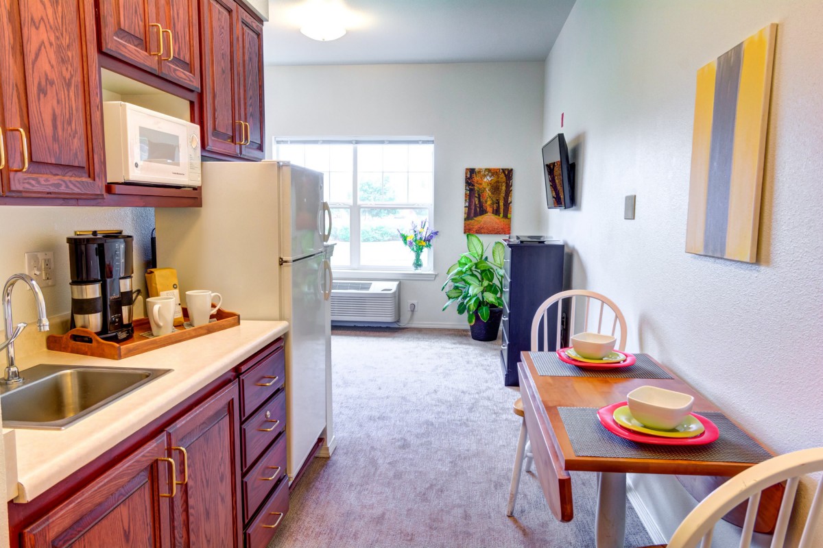 A cozy kitchen and dining area with wooden cabinets, a refrigerator, and a small dining table by the window.