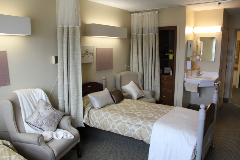 A cozy hospital room with a bed, armchair, and soft lighting.