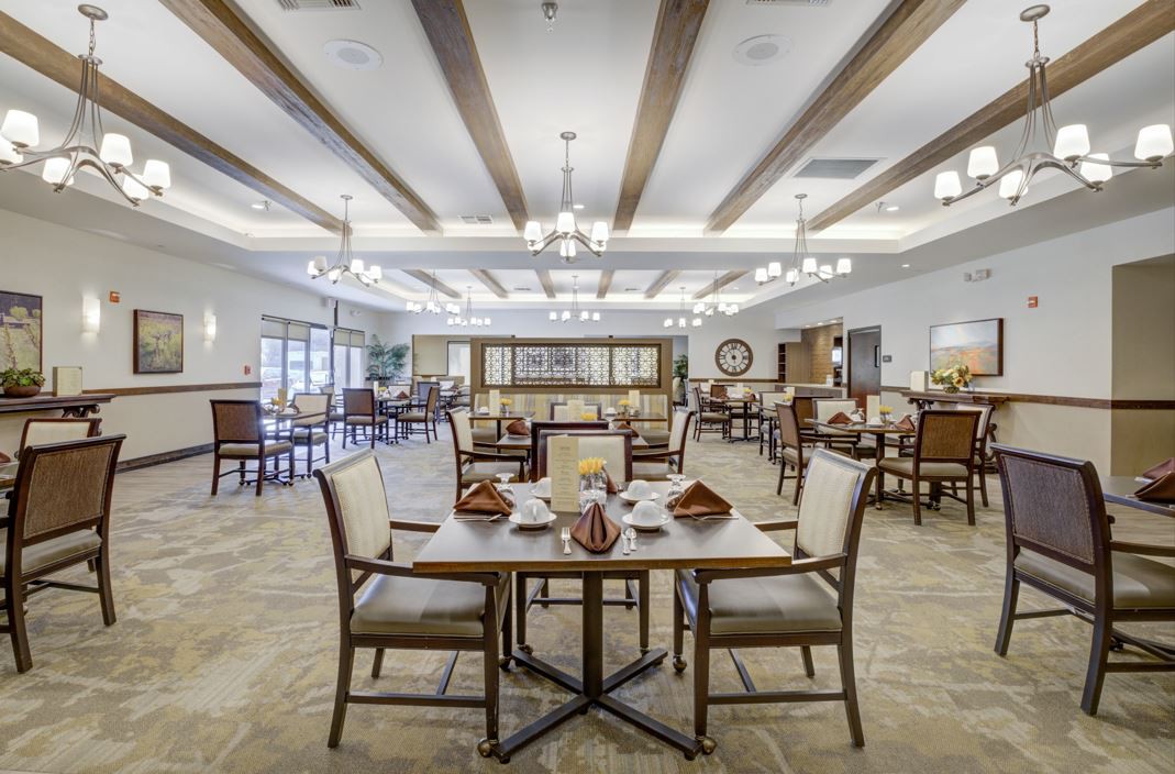 A spacious and elegantly decorated dining room with tables and chairs arranged neatly, featuring chandeliers and wooden ceiling beams.