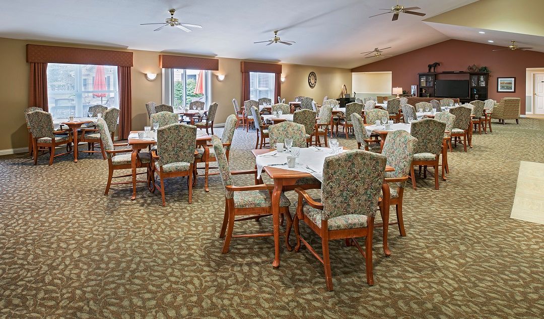 An empty dining room featuring neatly arranged tables and chairs with a carpeted floor and ceiling fans.