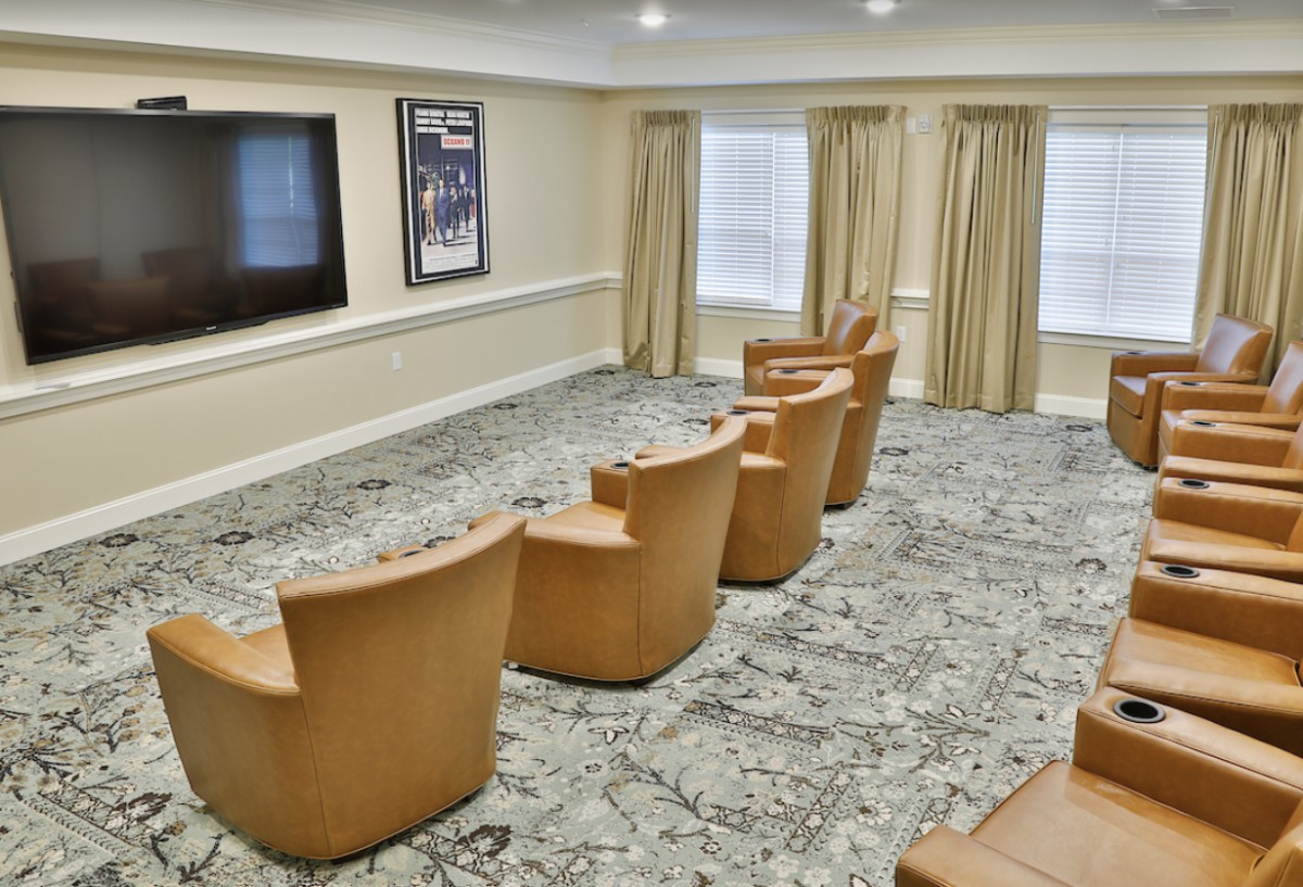 A cozy theater room with a row of comfortable chairs facing a large screen.