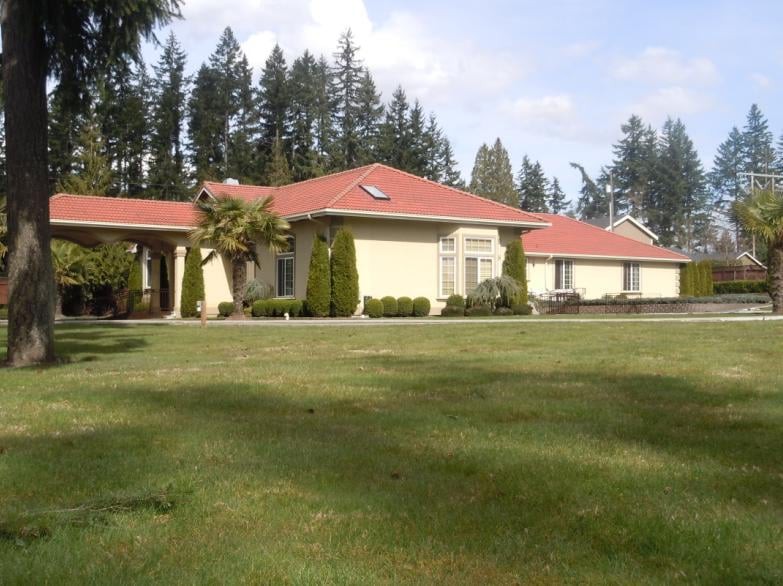 A suburban house with a red roof and expansive lawn surrounded by trees.