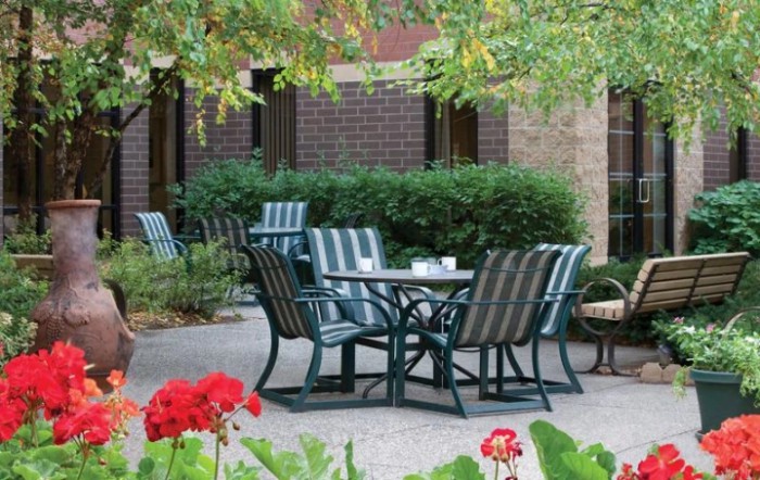 An outdoor patio area with metal chairs and a table surrounded by lush greenery.