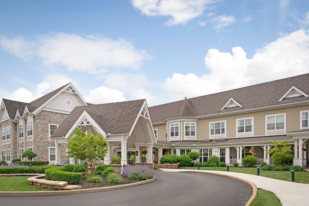 A large residential building with a landscaped driveway under a partly cloudy sky.