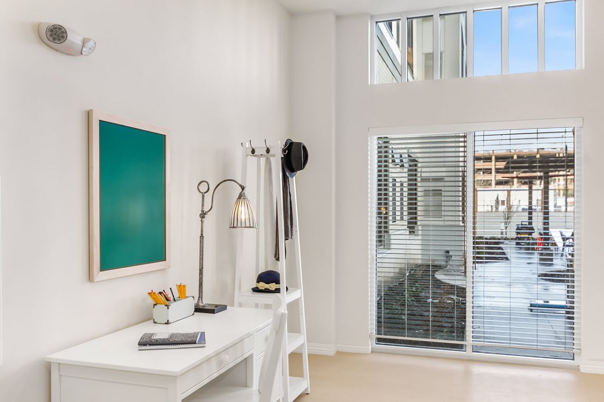 A modern and minimalist office space with a desk, lamp, artwork, and large window blinds.