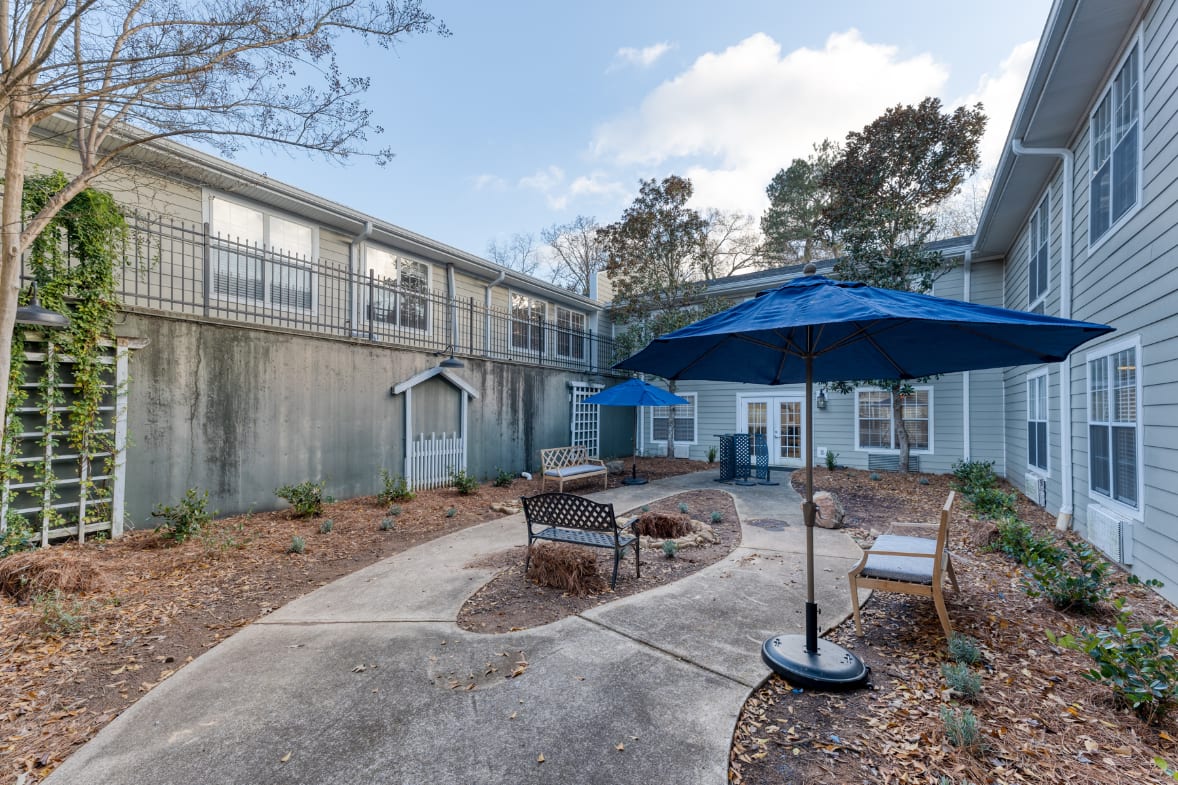 A serene outdoor courtyard with benches and an umbrella, surrounded by trees and adjacent to a building.