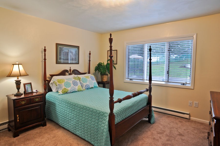 A cozy bedroom with a wooden four-poster bed, teal bedding, and a large window letting in natural light.