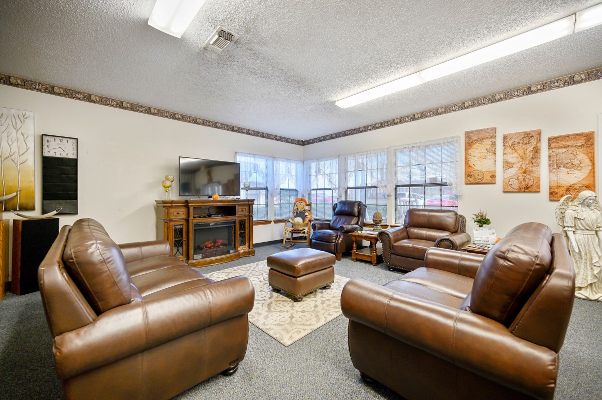 A cozy living room featuring leather sofas and a television, with ample natural light from large windows.