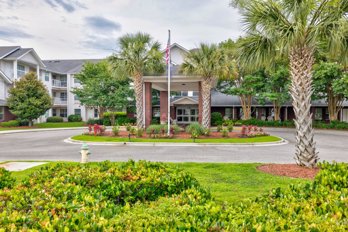 An inviting entrance of a residential building with well-maintained landscaping and a flagpole.