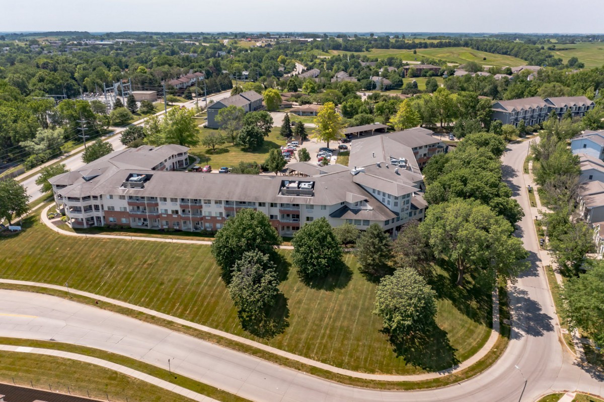 Aerial view of a large building surrounded by trees and roads in a suburban area.