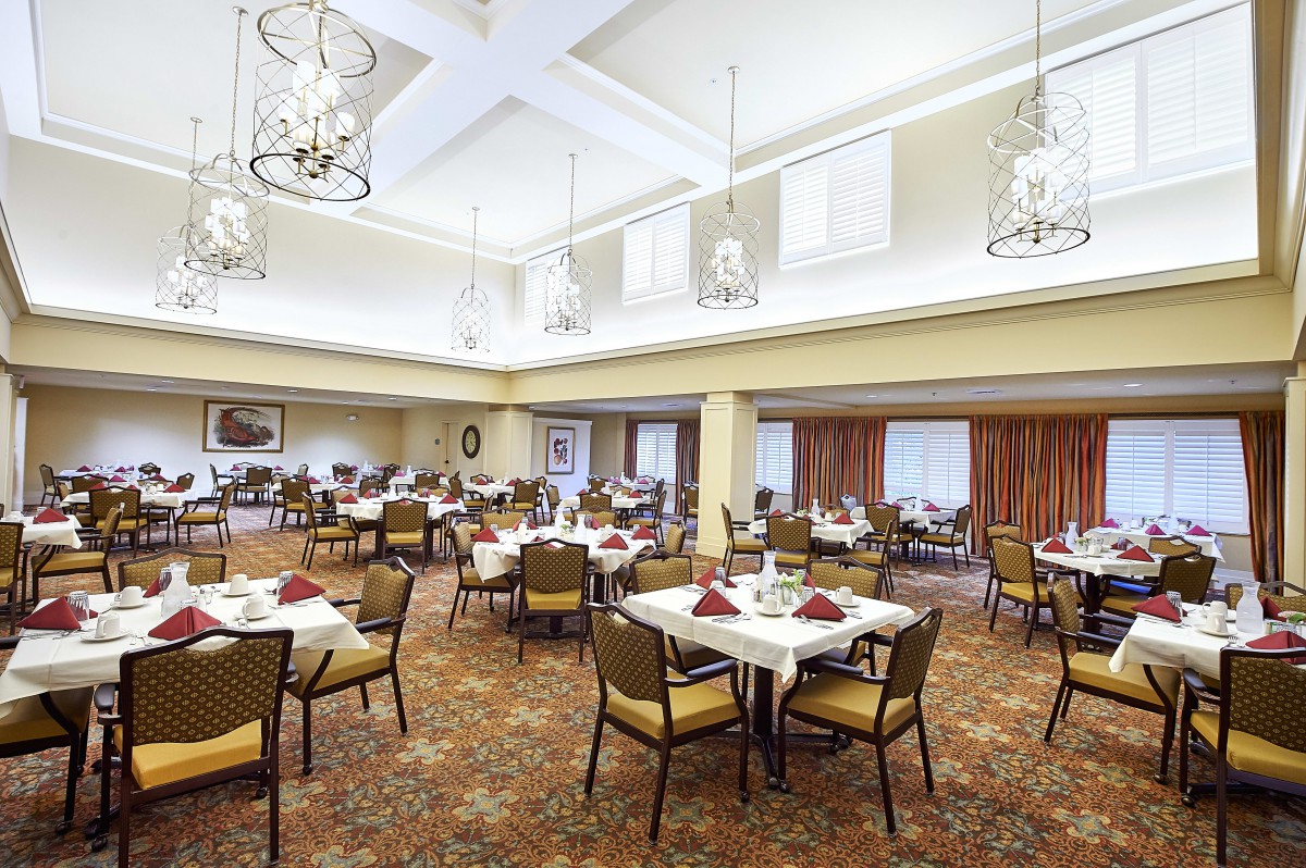 A spacious and elegant dining room with multiple set tables and chandeliers overhead.