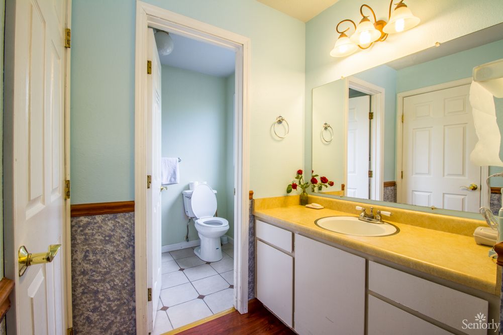 A bright bathroom featuring a yellow countertop, white cabinets, and a well-lit mirror.