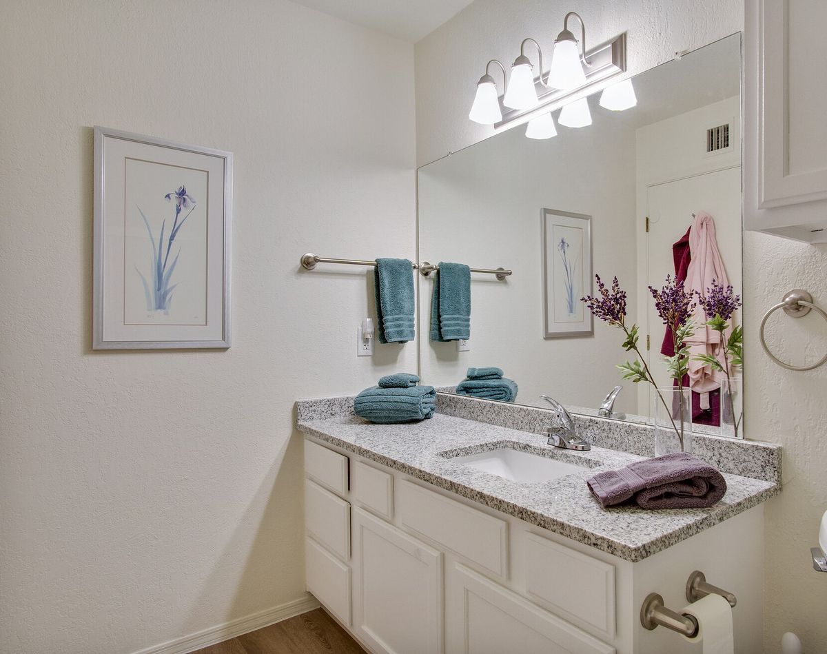 A modern bathroom with a large mirror, decorative flowers, and teal towels neatly arranged.