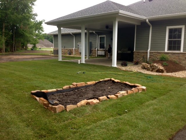 A backyard garden with a stone-bordered flower bed ready for planting.