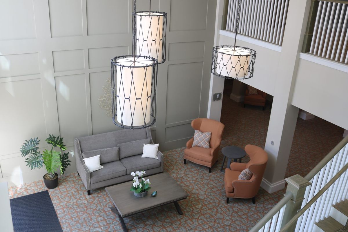 A modern living room with elegant chandeliers, a gray sofa, two orange armchairs, and a wooden coffee table.