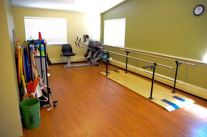 A rehabilitation room equipped with parallel bars and various exercise equipment.