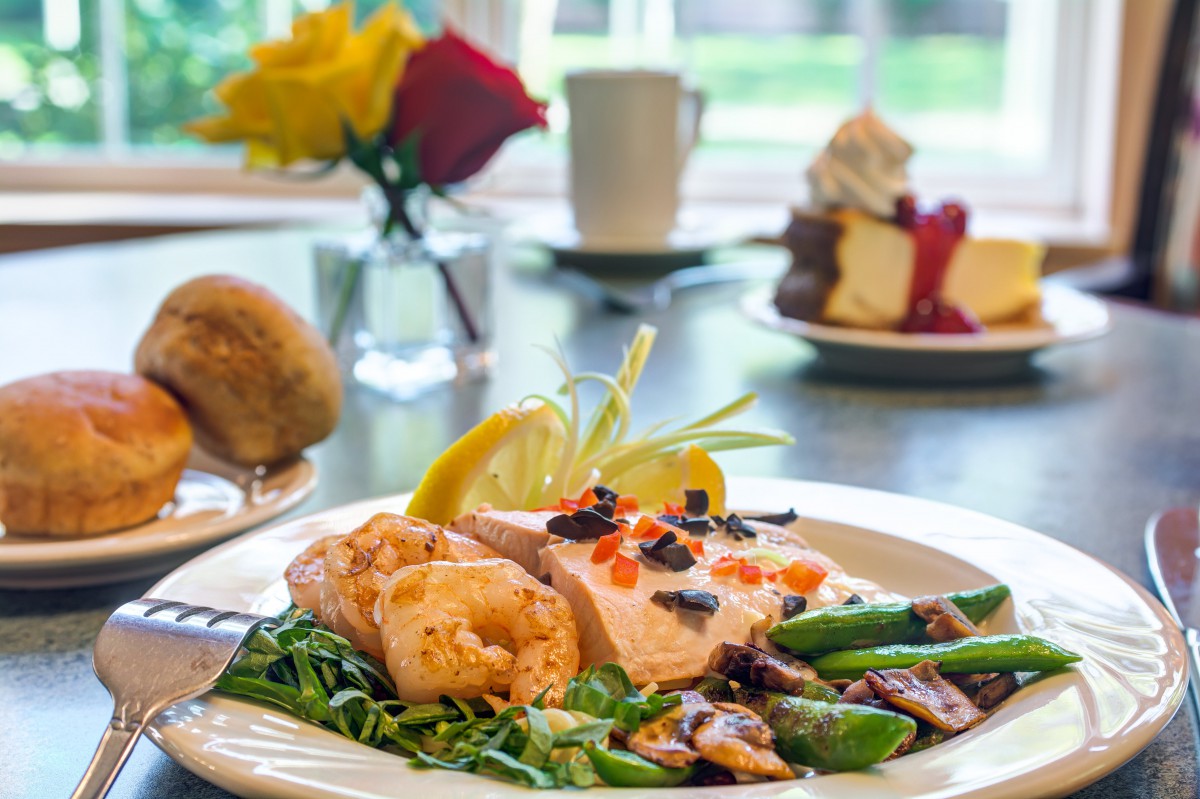 A gourmet meal featuring salmon with vegetables and a dessert in the background.