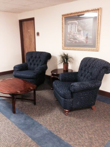 A cozy seating arrangement in a waiting area featuring two blue upholstered chairs and a wooden coffee table.