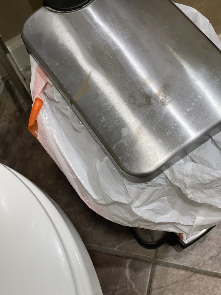 A stainless steel trash can with a white garbage bag inside.