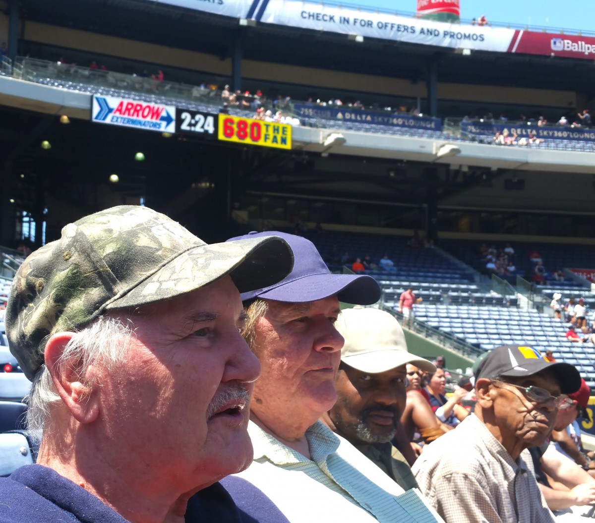 A group of spectators watching a baseball game at a stadium on a sunny day.