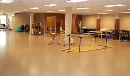 An interior view of a rehabilitation space equipped for physical therapy, featuring exercise bars and open floor space.