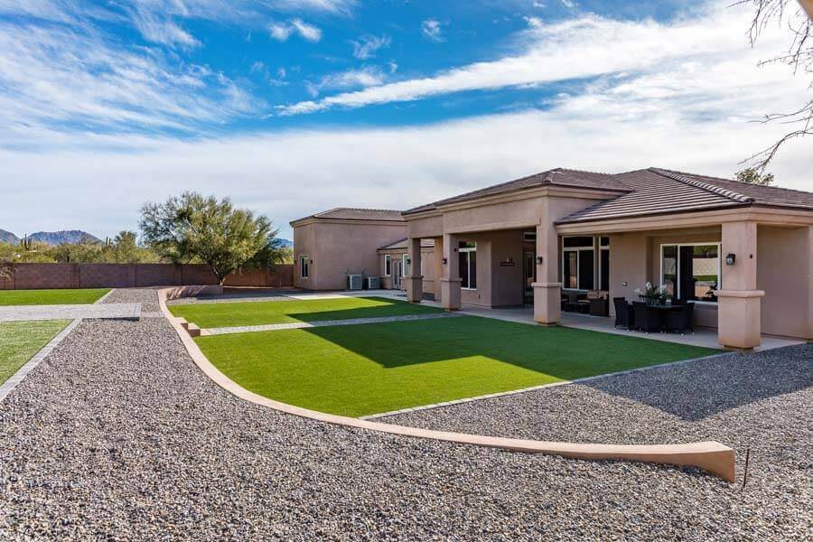 A sunny backyard featuring artificial grass and gravel landscaping around a modern house.