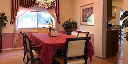 A dining room featuring a table with a red tablecloth, surrounded by chairs, decorated with a chandelier and curtains.