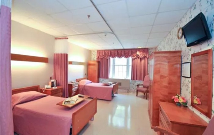 A spacious hospital room with two beds and pink decor.