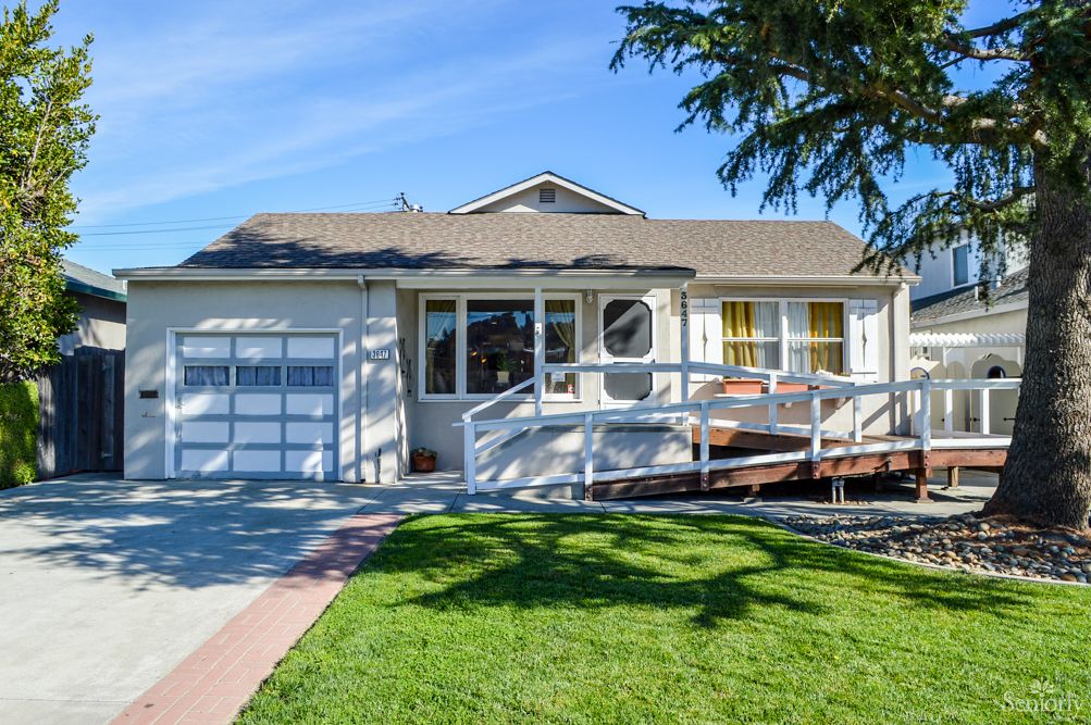 A quaint single-story house with a front ramp and garage on a sunny day.