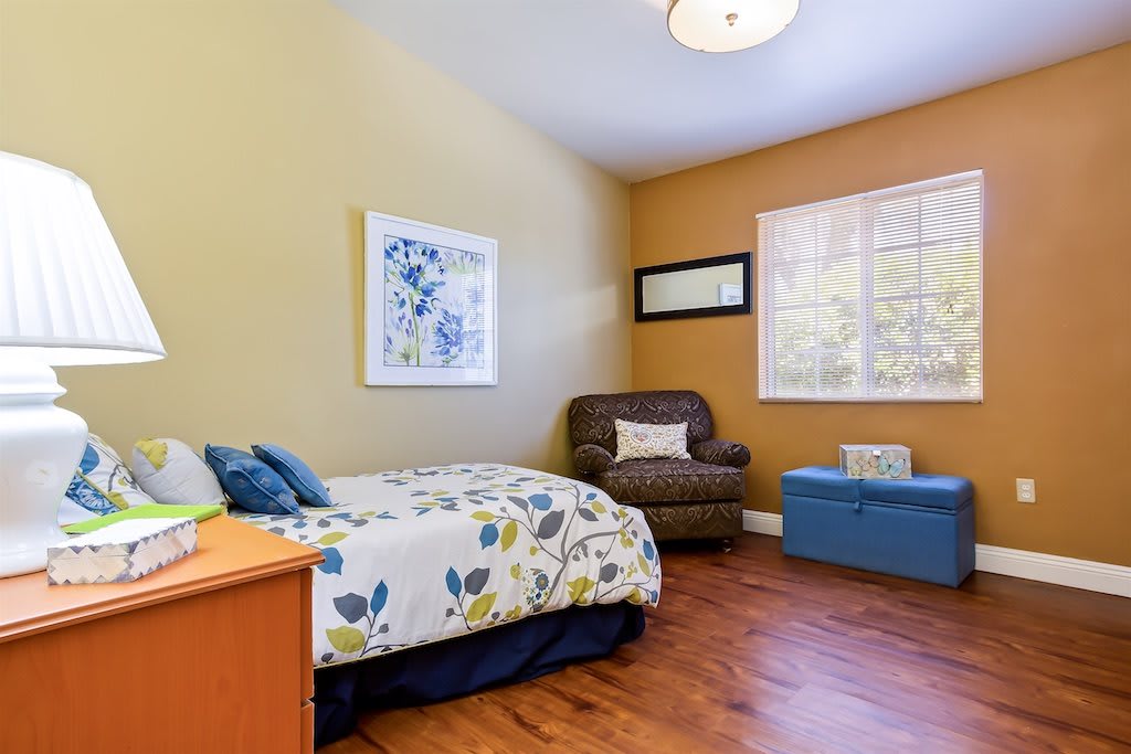 A cozy bedroom featuring a single bed with floral bedding, an armchair, and bright natural light.