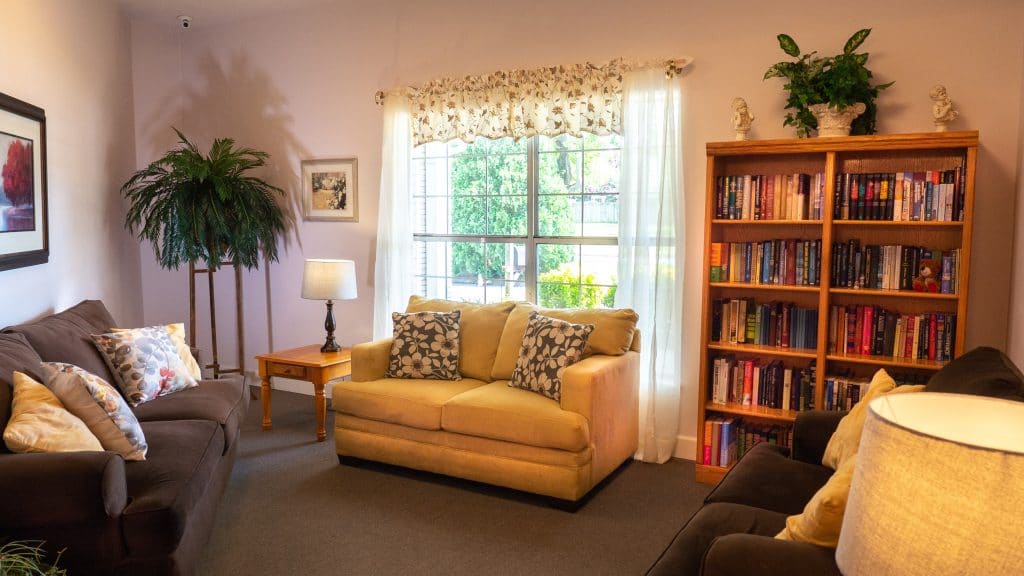 A cozy living room with a sofa, bookshelf, and large window letting in natural light.