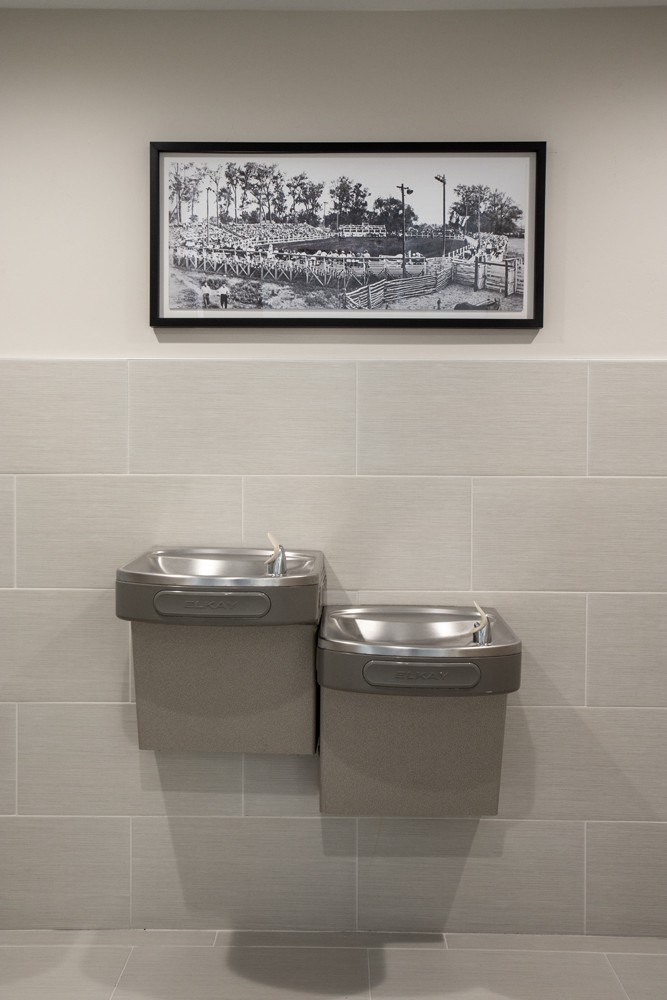 A pair of drinking fountains mounted on a tiled wall with a historical photograph hanging above.