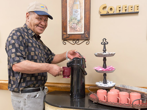 A cheerful elderly man serving coffee in a cozy kitchen setting.