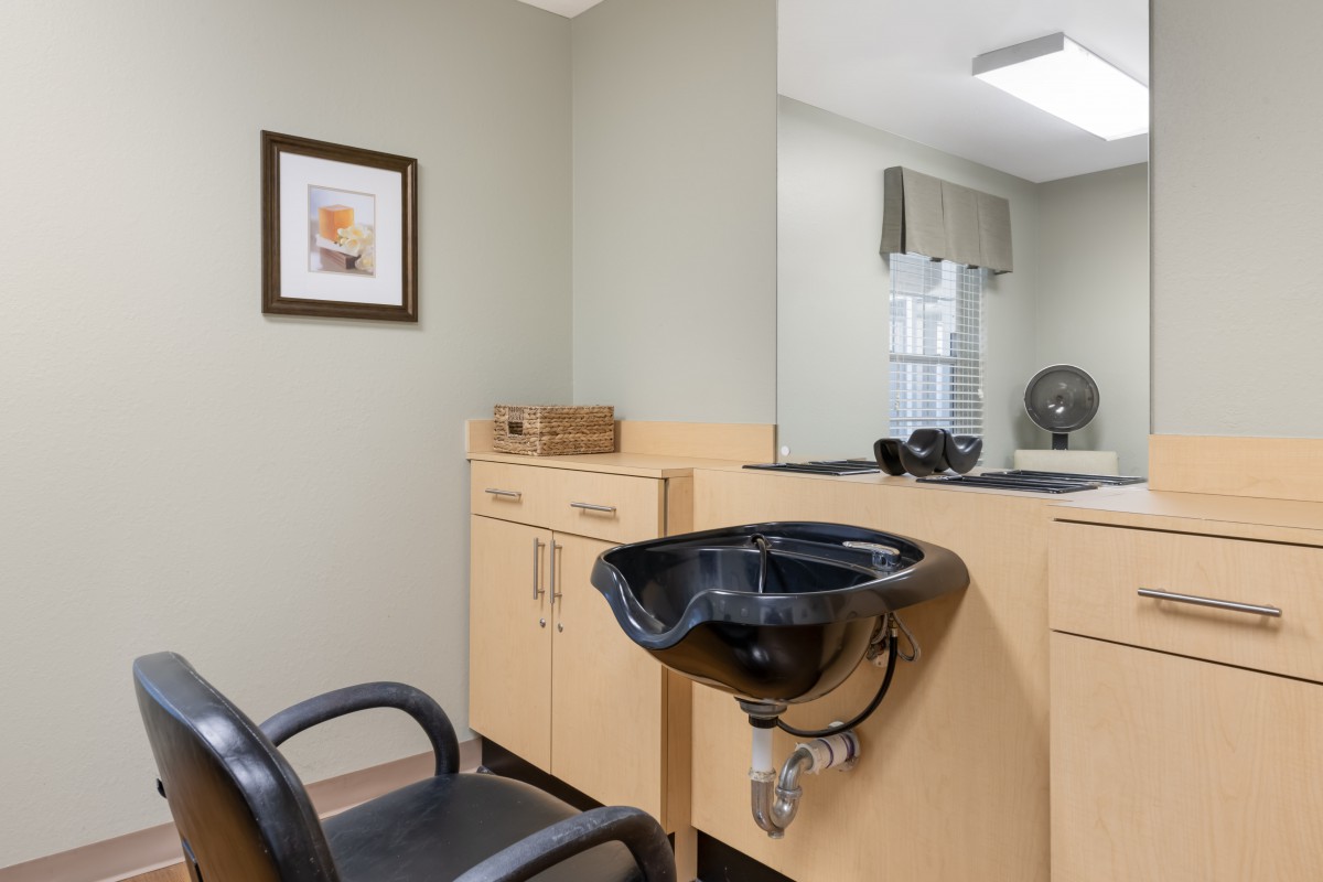 A hair salon setup with a chair, sink, and wooden cabinets.