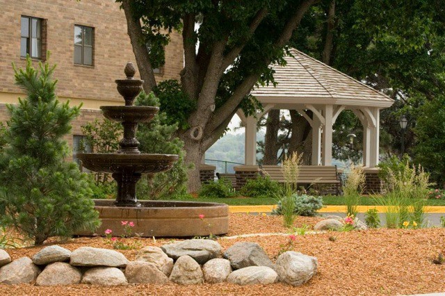 A peaceful garden setting featuring a three-tiered fountain and a wooden gazebo surrounded by greenery.