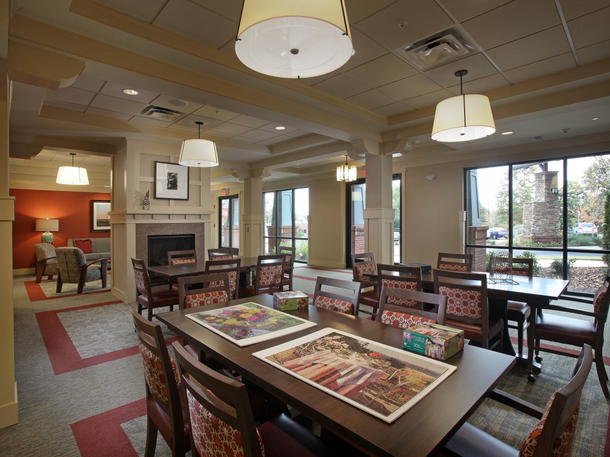 A cozy dining area with tables and chairs arranged under ceiling lights, featuring large windows that allow natural light to illuminate the space.