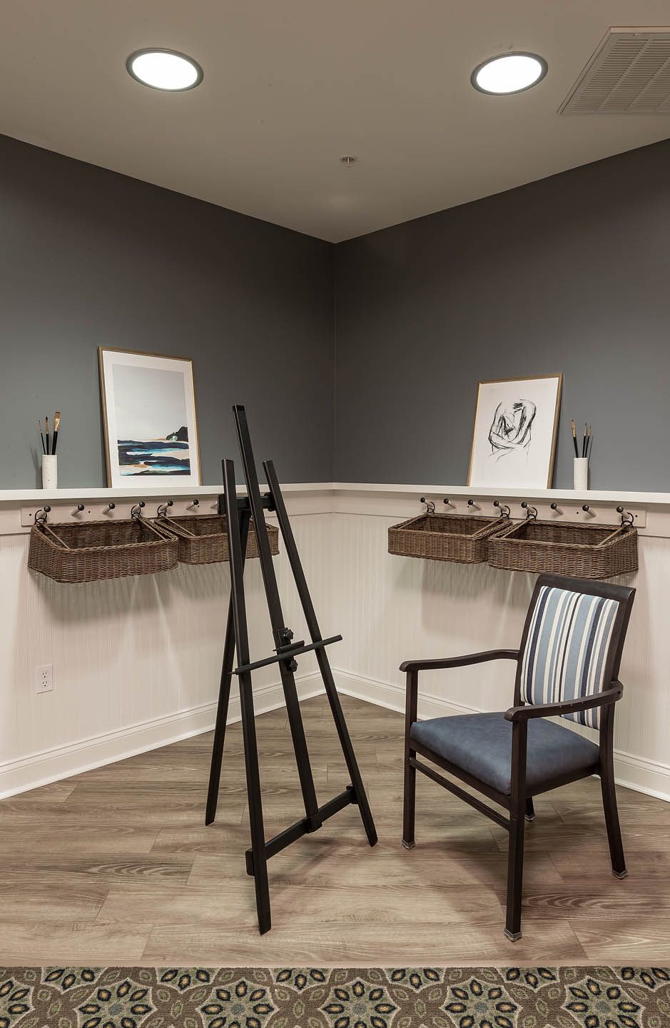 A cozy room featuring art displays with wicker baskets, an easel, and a comfortable chair on a wooden floor.