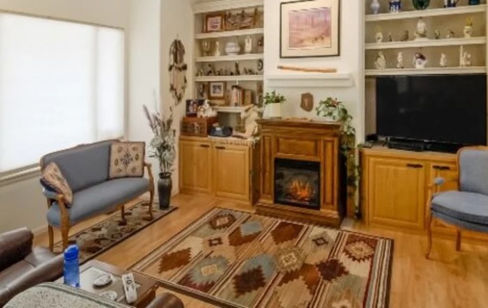 A cozy living room with a fireplace, patterned carpet, and decorative shelves.