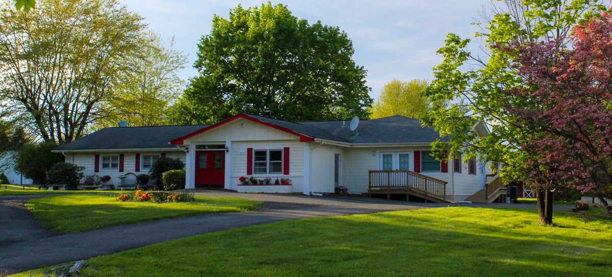 A single-story house with a red door and shutters, surrounded by trees and a well-maintained lawn.