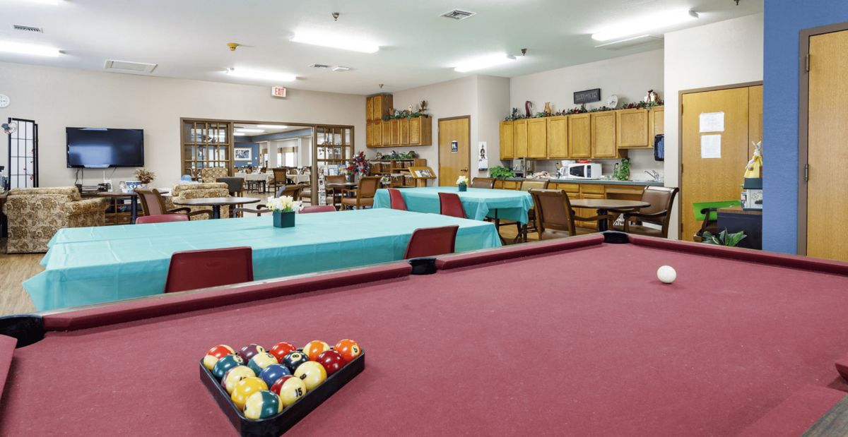 A spacious recreation room featuring a red pool table and several tables with teal coverings, ideal for community gatherings and leisure activities.