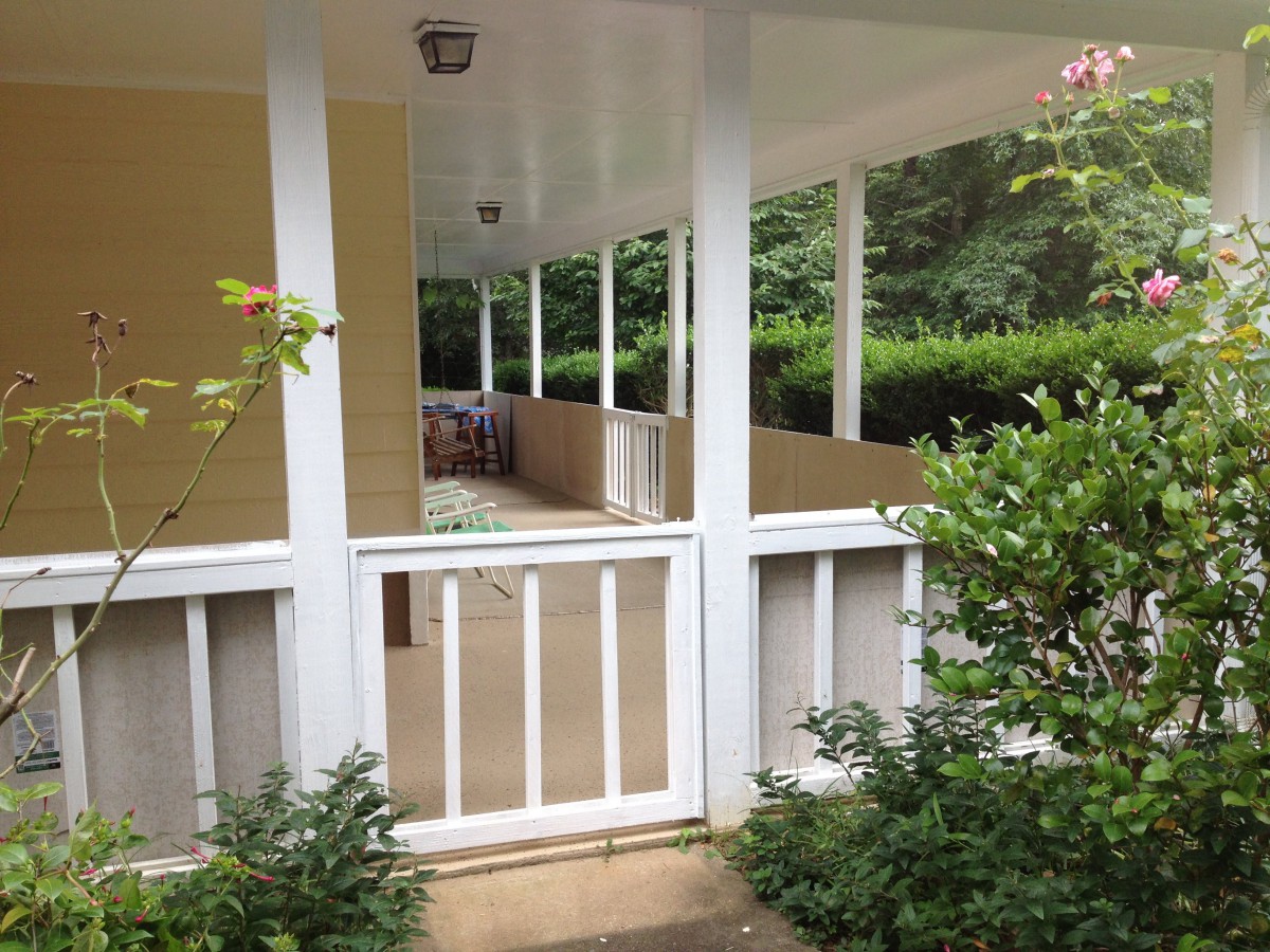 A covered porch with a gate, surrounded by greenery.