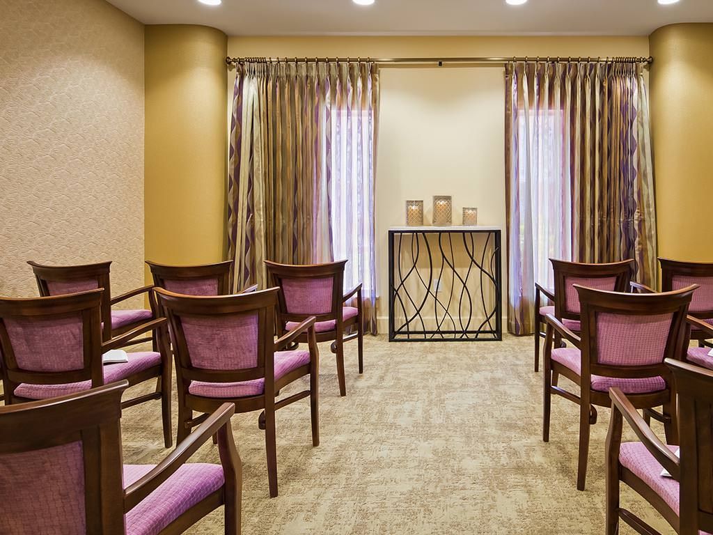 A small meeting room setup with chairs facing a decorative stand against curtained windows.