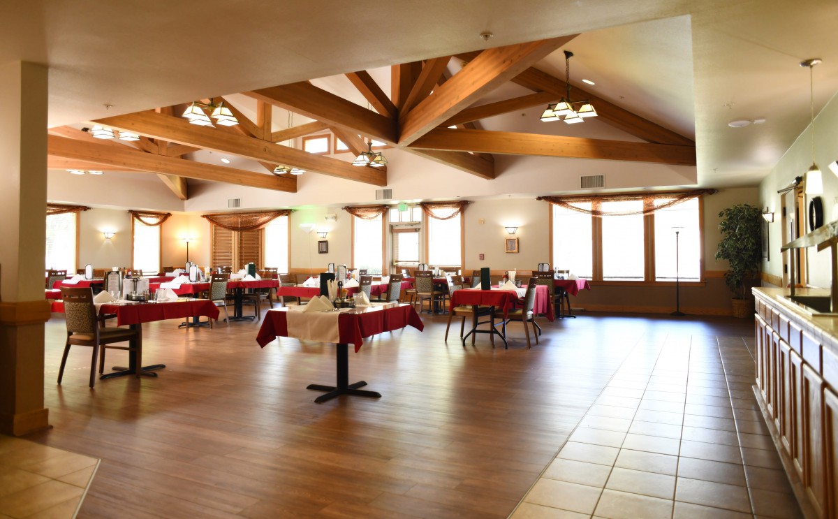 A spacious restaurant interior featuring wooden beams, tables, and chairs.