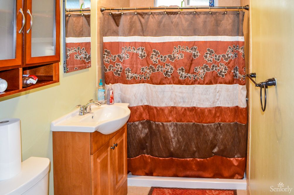 A bathroom featuring a colorful shower curtain, a sink with wooden cabinetry, and a wall-mounted mirror.