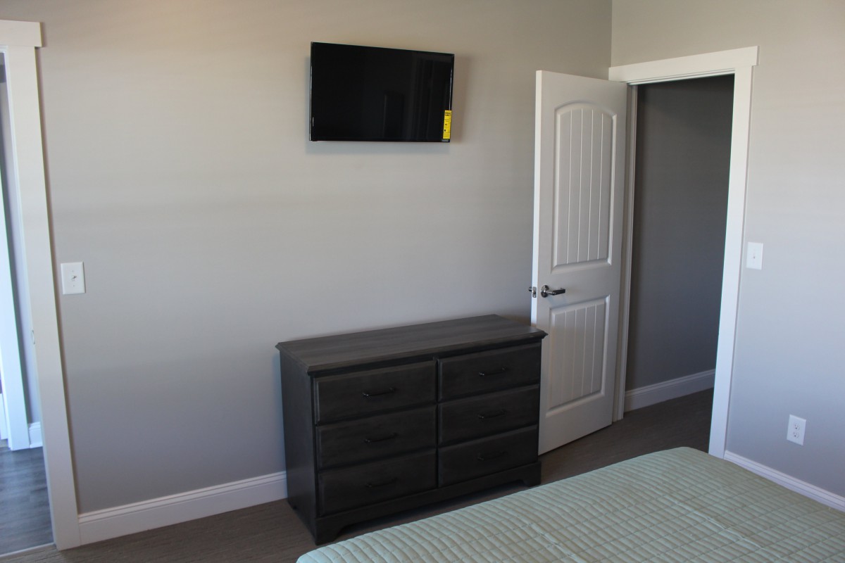 A minimalist bedroom with a wall-mounted TV and a dark dresser.